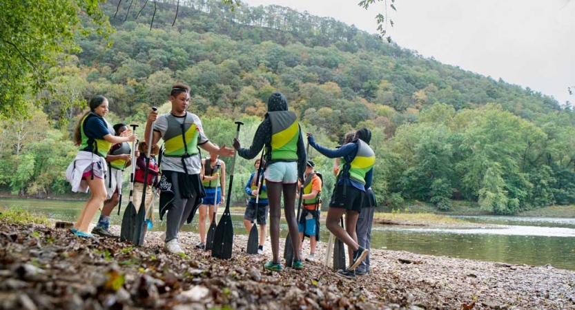 a group of teens stand on a shore on a canoeing expedition near baltimore